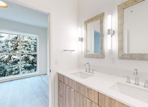 A bathroom with a large mirror and a window overlooking a snowy landscape at One West Drive Apartments, Excelsior