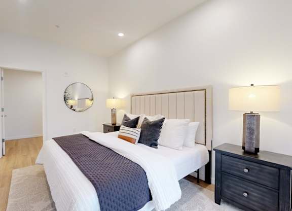 A bedroom with a large bed, a nightstand, and a mirror on the wall.