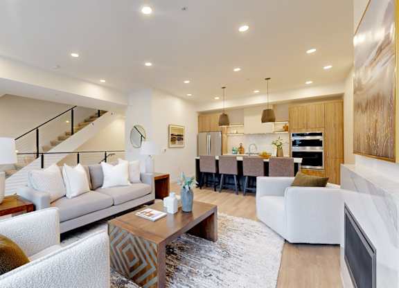 A modern living room with a staircase and a kitchen in the background.