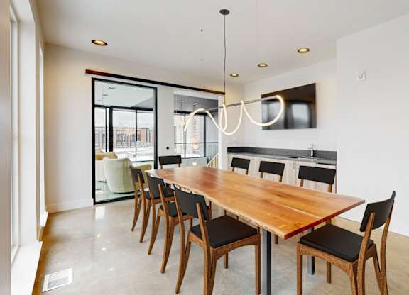 A long wooden dining table with chairs and a chandelier hangs in a white room.