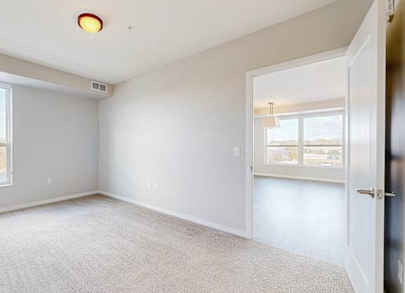 A spacious, empty room with a large window and a door leading to another room.