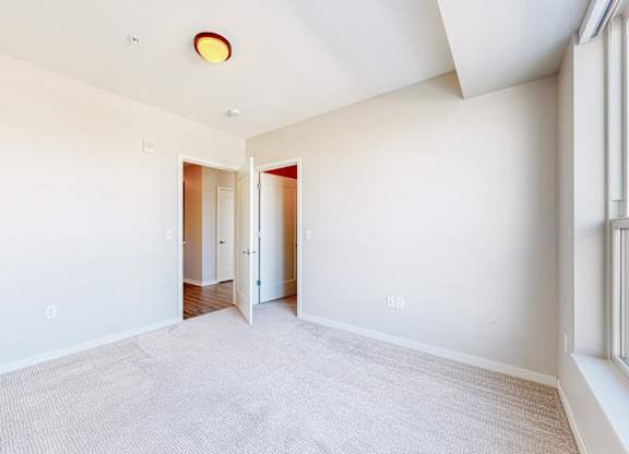 A large, empty room with a carpeted floor and a window on the right side.