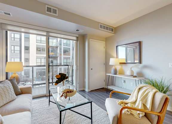 A living room with a white sofa, a glass coffee table, and a large window.