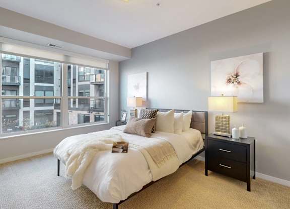 A bedroom with a large bed, a nightstand, and a window overlooking a building.