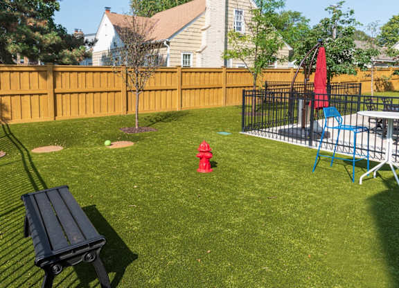 A backyard with a black bench and a red fire hydrant.
