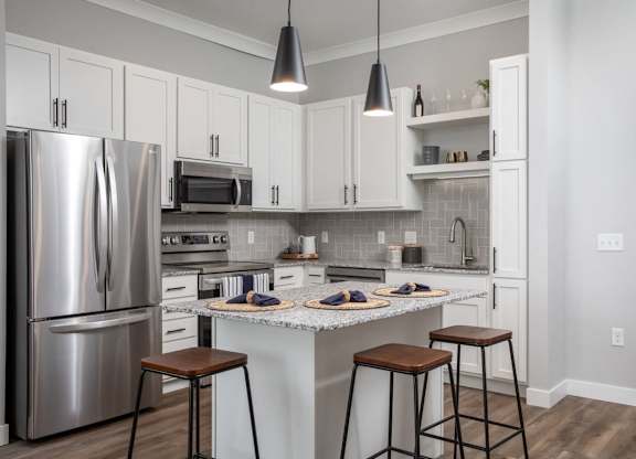 A kitchen with a refrigerator, microwave, oven, and bar stools.at The Edison at Maple Grove, Maple Grove, MN 55311