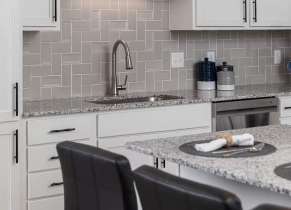 A kitchen with white cabinets and a grey backsplash.at The Edison at Maple Grove, Maple Grove, 55311