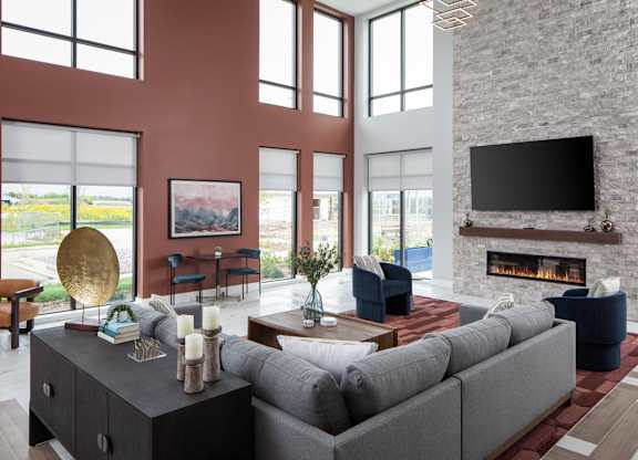 A modern living room with a grey sofa, a fireplace, and a large window.at The Edison at Maple Grove, Minnesota, 55311