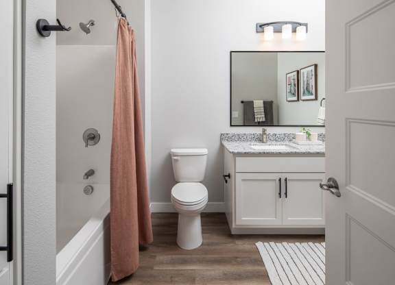 A bathroom with a toilet, sink, and a pink towel hanging on the shower rod.at The Edison at Maple Grove, Maple Grove, 55311