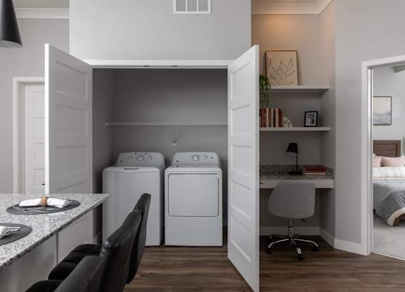 A laundry room with a washer and dryer is open to a bedroom.at The Edison at Maple Grove, Minnesota