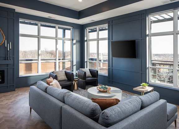 A grey couch is in front of a large window in a room with a fireplace.at The Edison at Maple Grove, Maple Grove Minnesota
