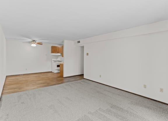 an empty living room with a ceiling fan and a kitchen in the background