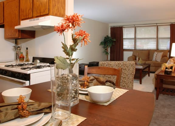a living room with a wooden table and a kitchen in the background at Point of America Apartments,Brooklyn Park, Minnesota