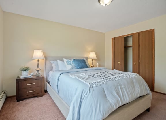 a bedroom with a large bed and a nightstand with two lamps at Point of America Apartments,Brooklyn Park, Minnesota