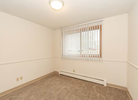 A room with a window covered by white blinds and a radiator on the floor.