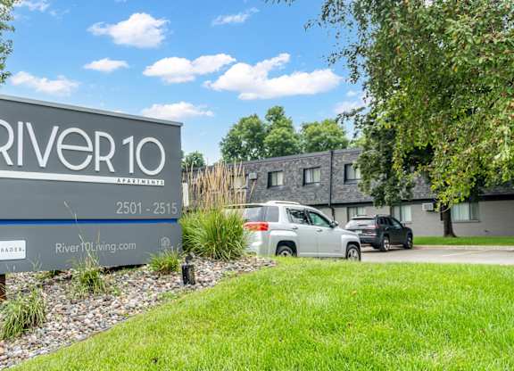 A sign for River10 is in front of a grassy area and some trees.