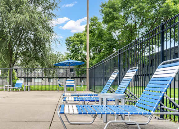 A poolside area with blue lounge chairs and a fence.