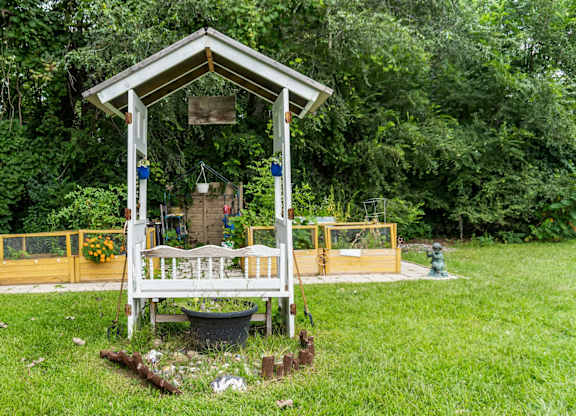 A small wooden structure with a porch and a yellow fence is surrounded by greenery.
