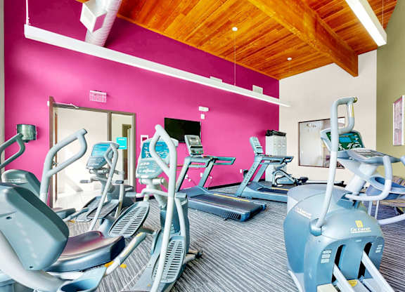 A gym with exercise equipment and a pink wall.