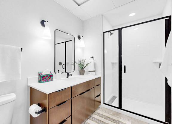 A white bathroom with a wooden vanity and a glass shower door.