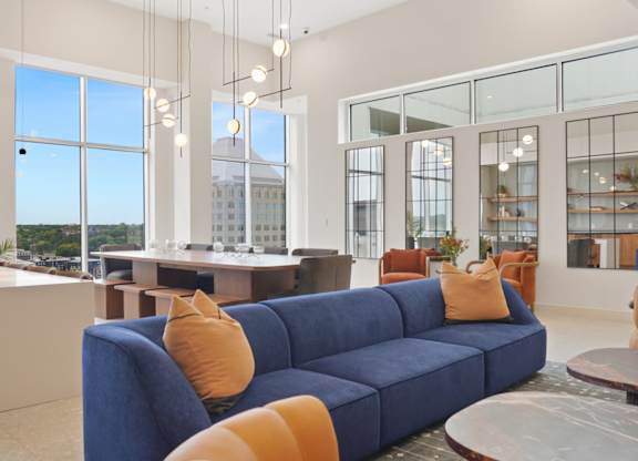 A blue couch with orange pillows is in the middle of a room with a kitchen in the background.