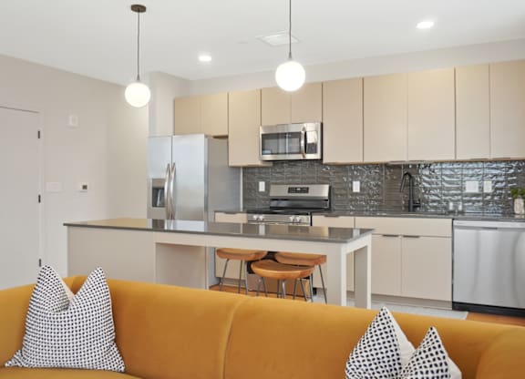 A modern kitchen with a yellow couch in the foreground.