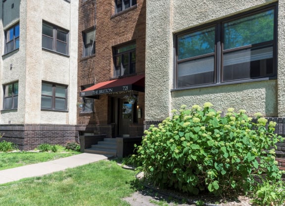 the front of a brick apartment building with a sidewalk and bushes