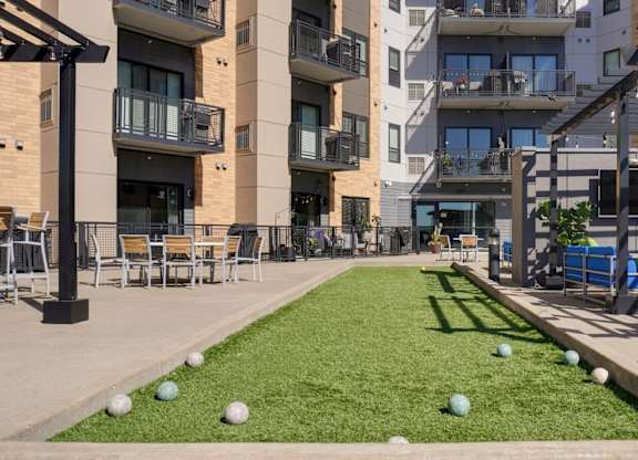 A grassy area with a few chairs and a bench in front of apartment buildings.