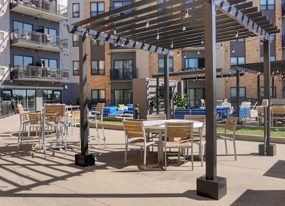 A patio with chairs and tables is shaded by a pergola.