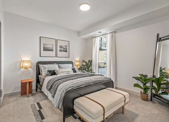 A bedroom with a large bed, a bench, and a potted plant.