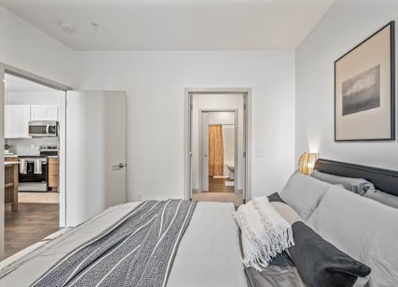 A bedroom with a large bed and a kitchen area in the background.