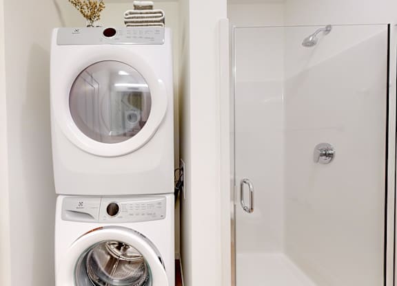 A white washing machine and dryer stacked on top of each other in a small laundry room.