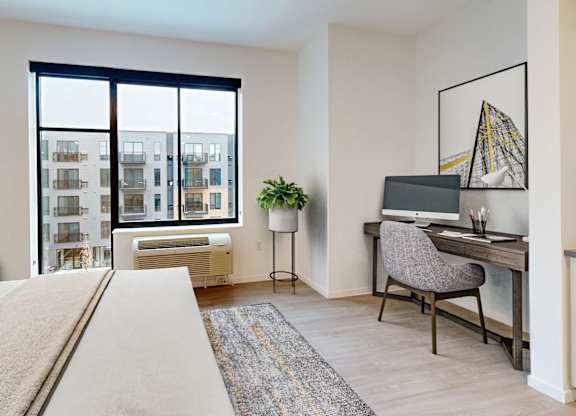 A bedroom with a large bed, a desk with a chair, and a window overlooking a cityscape.