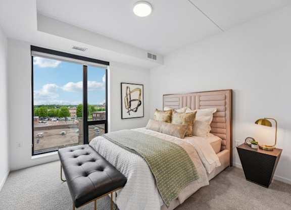 A bedroom with a large bed, a bench, and a window overlooking a parking lot.