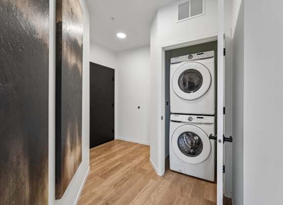 A white washing machine is in a small room with a wooden floor.