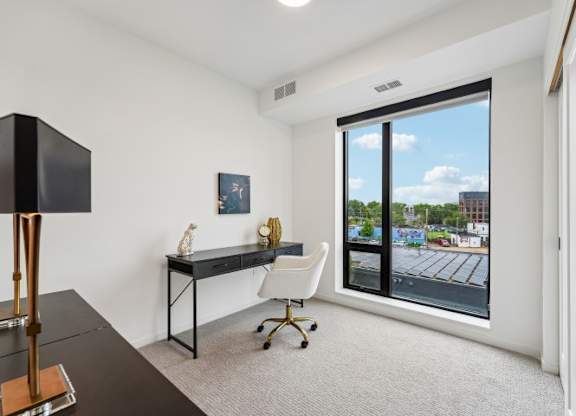 A room with a desk and chair with a window showing a parking lot.