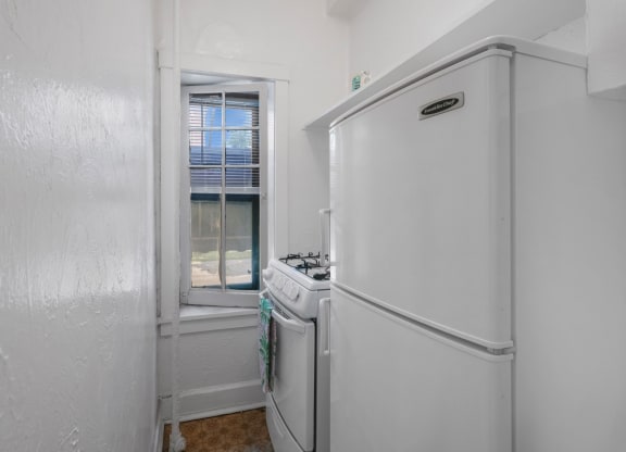 a small white kitchen with a window and a white refrigerator