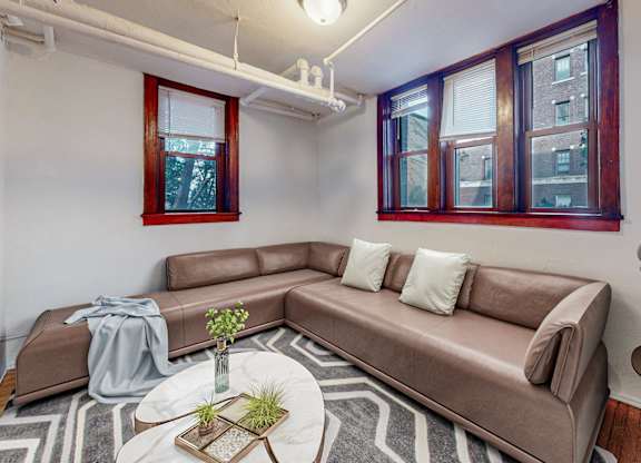 A brown couch with a grey throw is in a room with a round table and a floor lamp.