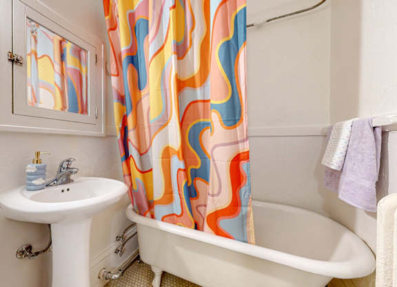 A bathroom with a white tub, sink, and shower curtain.