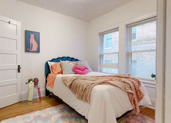 A bedroom with a bed, pillows, and a picture of a cat on the wall.