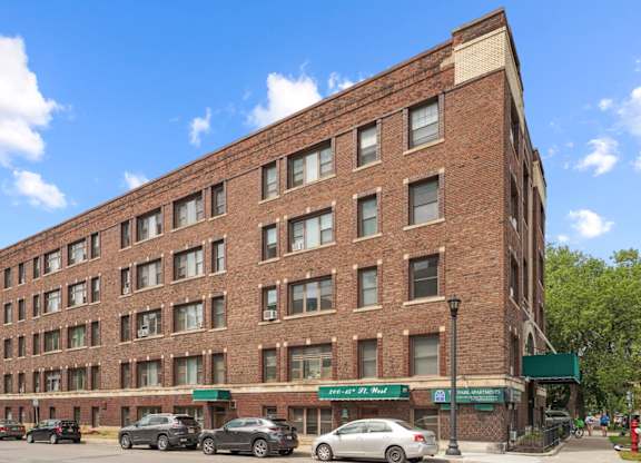 A large brick building with a green awning and cars parked in front.