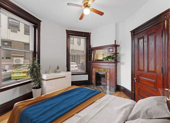 A bedroom with a bed, a fireplace, and a window overlooking a street.