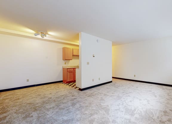 a bedroom with a white wall and a white door with a kitchen in the background