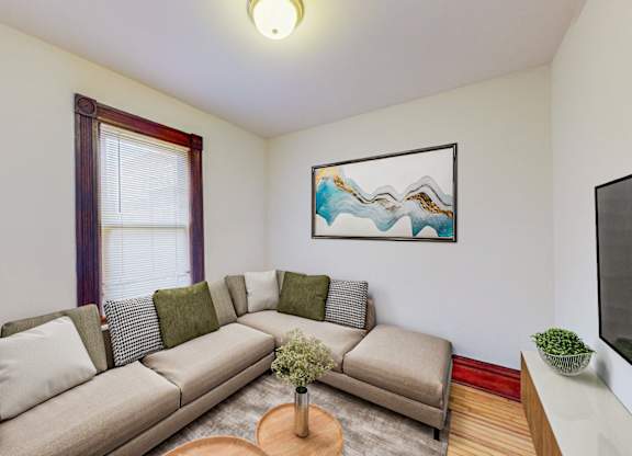 A living room with a grey couch, a painting on the wall, and a small table with a vase of flowers.
