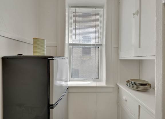 A black refrigerator sits next to a window in a kitchen.
