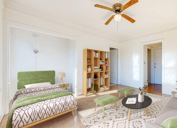 A bedroom with a bed, a couch, a bookshelf, and a ceiling fan.