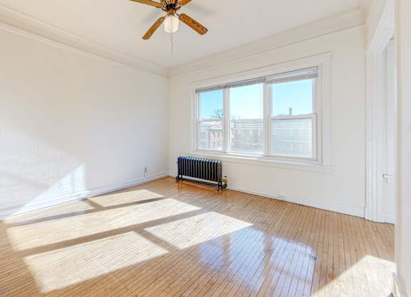 A room with a ceiling fan and a window with a view of buildings outside.