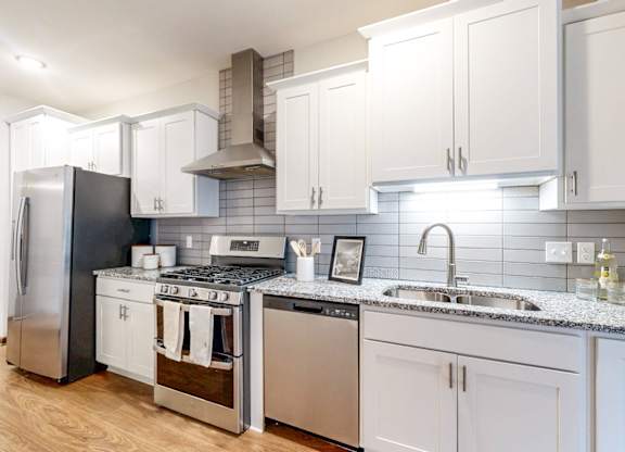 A modern kitchen with a stainless steel refrigerator, a stove with a cooking pot on it, and a sink with a faucet.