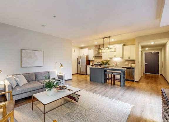 A modern living room with a grey sofa, wooden chairs, and a coffee table.