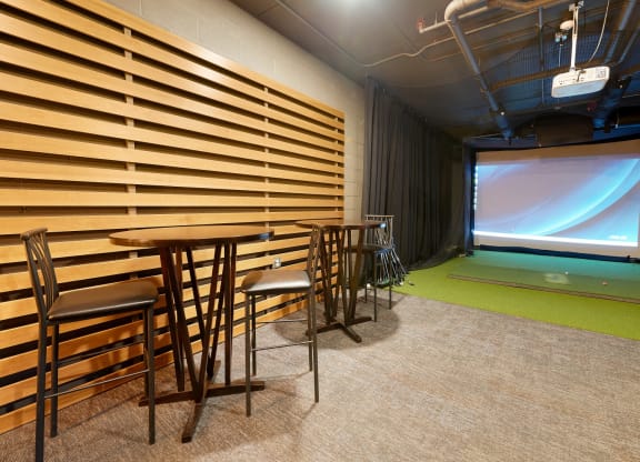 golf simulator room with chairs, artificial turf and a projector screen